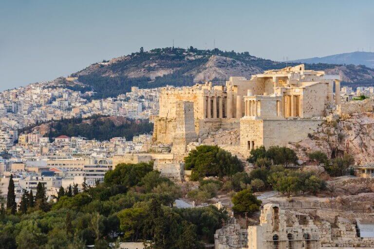 Check out the best Athens hotels for families recommended by top family travel blog Marcie in Mommyland. Image of Entrance to Ancient Acropolis in rays of sunset. Athens Greece