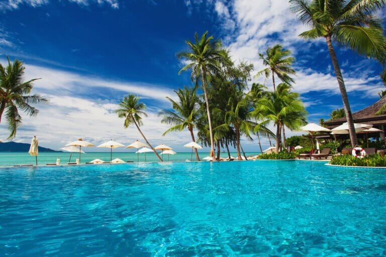Check out the best Phuket resorts for families recommended by top family travel blog Marcie in Mommyland. Image of Large infinity swimming pool on the beach with palm trees