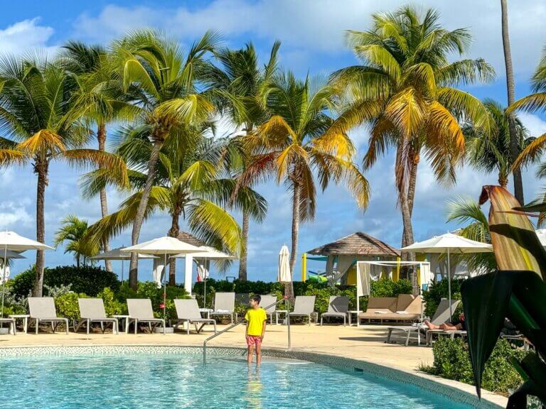 Check out this comparison of Hawaii vs Caribbean by top family travel blog Marcie in Mommyland. Image of a boy in a pool at a Caribbean resort.