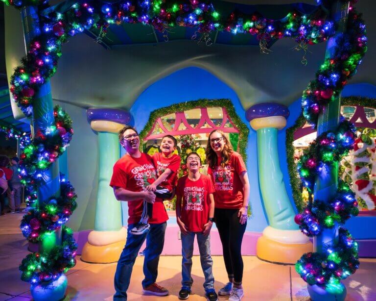 Find out whether or not it's worth visiting Universal Studios at Christmas with tips by top family travel blog Marcie in Mommyland. Image of Marcie Cheung and her family posing with Christmas lights at Grinchmas at Universal Studios Orlando. Photo credit: Sees the Day Photography