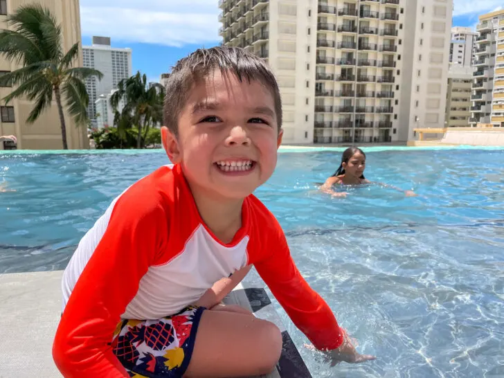 Check out the best Waikiki resorts for families recommended by top family travel blog Marcie in Mommyland. Image of a boy at the pool at the Alohilani Resort in Waikiki