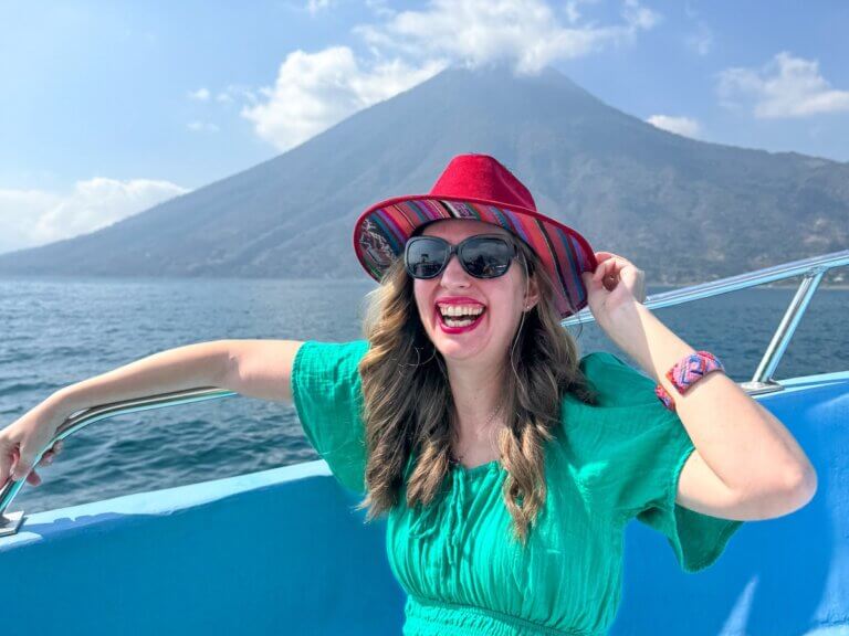 Check out this list of things to do in Lake Atitlan Guatemala by top travel blog Marcie in Mommyland. Image of a woman on a boat with a volcano behind her.