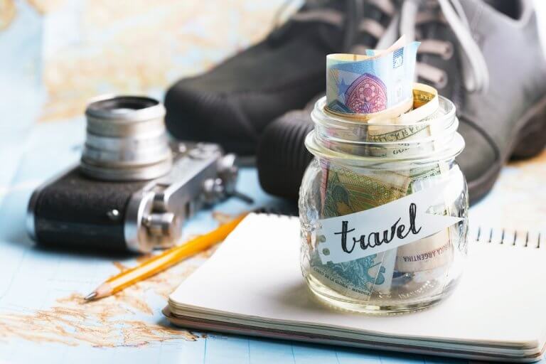 Find out my top budget travel tips for families! Image of a camera, boots, maps, and a jar of cash