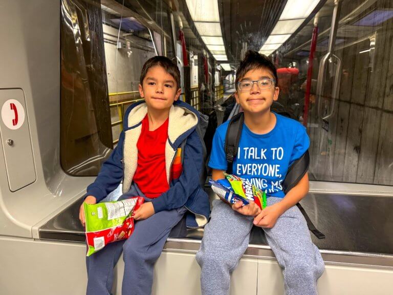 Find out family travel tips for talking about the realities of travel with your kids. Image of two boys sitting on an airport train in Seattle
