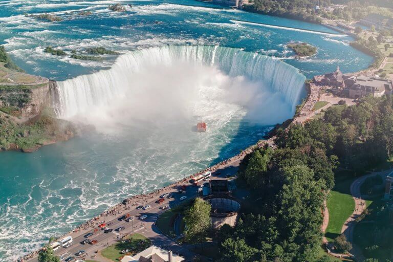 Find out the top places to add to your USA bucket list according to top family travel blog Marcie in Mommyland. Image of Aerial top landscape view of Niagara Falls between United States of America and Canada. Horseshoe of Canadian waterfall on sunny day. Water tour boat at famous tourist landmark