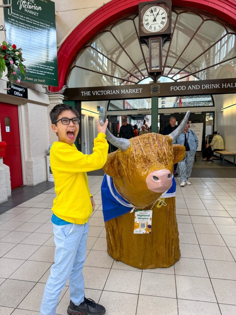 Image of a boy with a Highland Coo statue in Victorian Market in Inverness