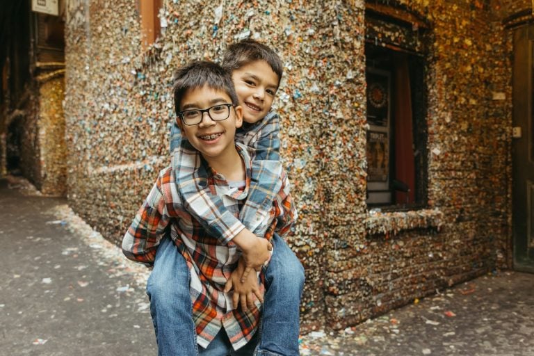 Find out the top 15 things to do before your kids turn 18 recommended by top family travel blog Marcie in Mommyland. Image of 2 boys at the gum wall at Pike Place Market in Seattle