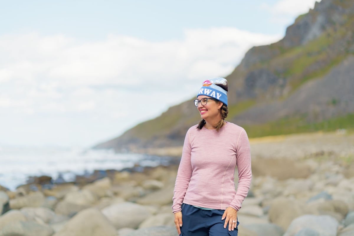 Find out the best Norway packing tips for summer from top travel blogger Marcie Cheung. Image of Marcie Cheung wearing wool layers on a beach in the Lofoten Islands.